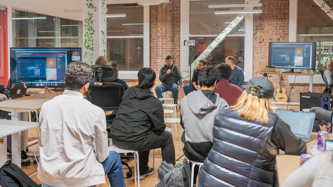 Homebrew Club community gathering with talks, code on screens, and a guitar